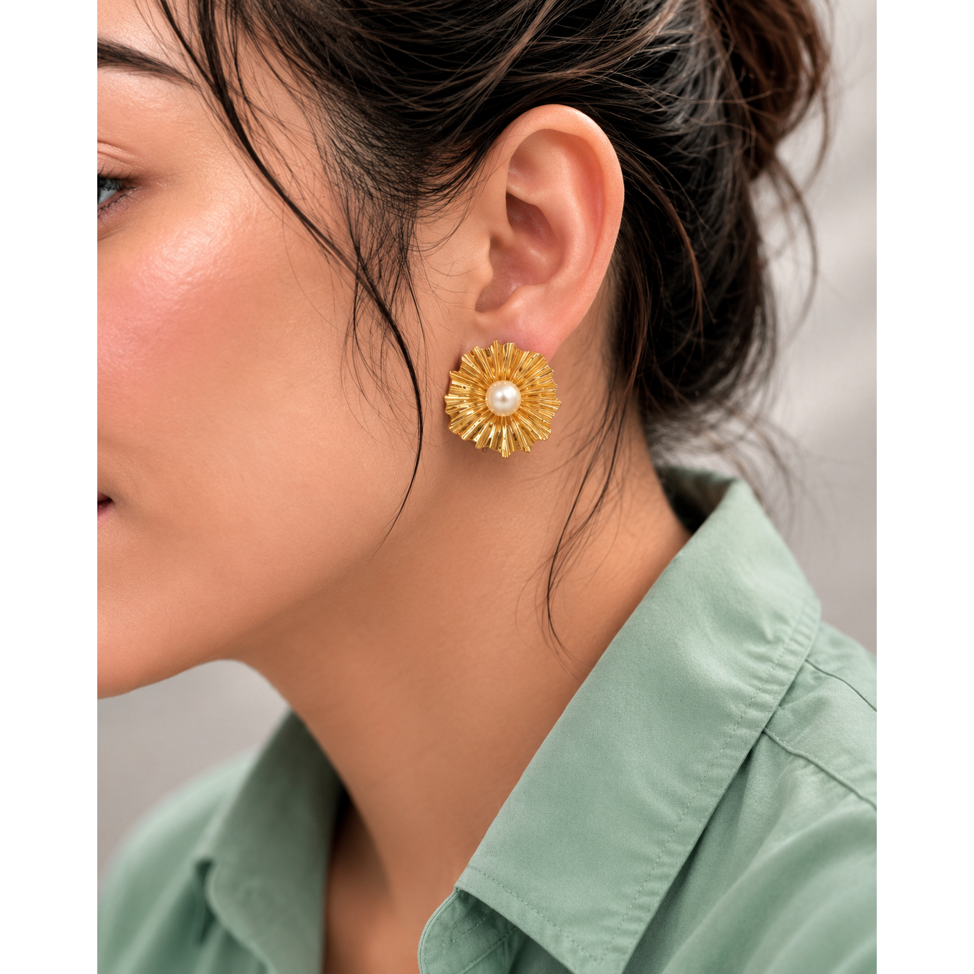Close-up of a woman wearing a gold floral earring with a pearl center.