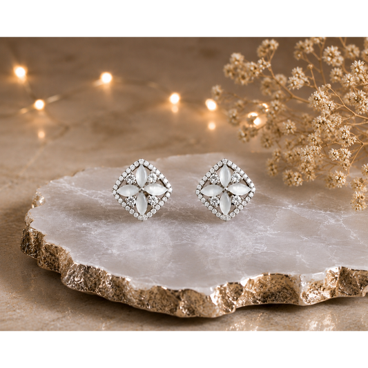 Silver floral stud earrings with white petal stones displayed on a luxury white agate stone slab with warm decorative lighting.
