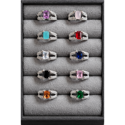 Silver tone adjustable square cut artificial gemstone rings arranged in grey velvet box featuring pink, turquoise, red, blue, green, black and clear stone variants