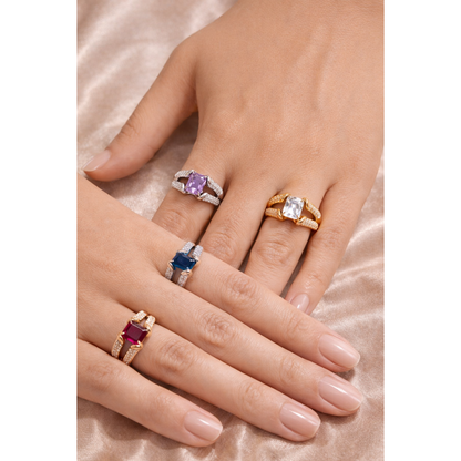 Adjustable gemstone rings displayed on female hands featuring gold and silver tone bands with square-cut stones in purple, blue, clear, and deep red, photographed on soft champagne satin fabric background showing fashion jewellery styling and multiple colour variants of the same ring design