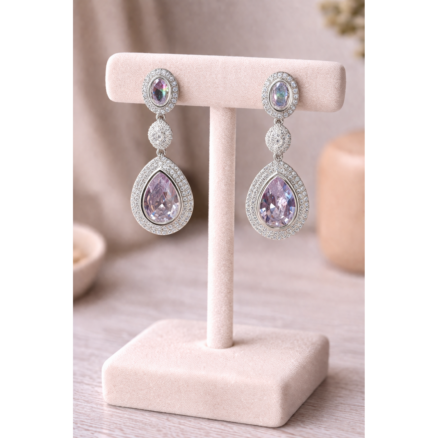 High-definition product photo of silver drop earrings with clear crystal stones displayed on a jewelry stand, featuring pavé detailing and a modern statement design.