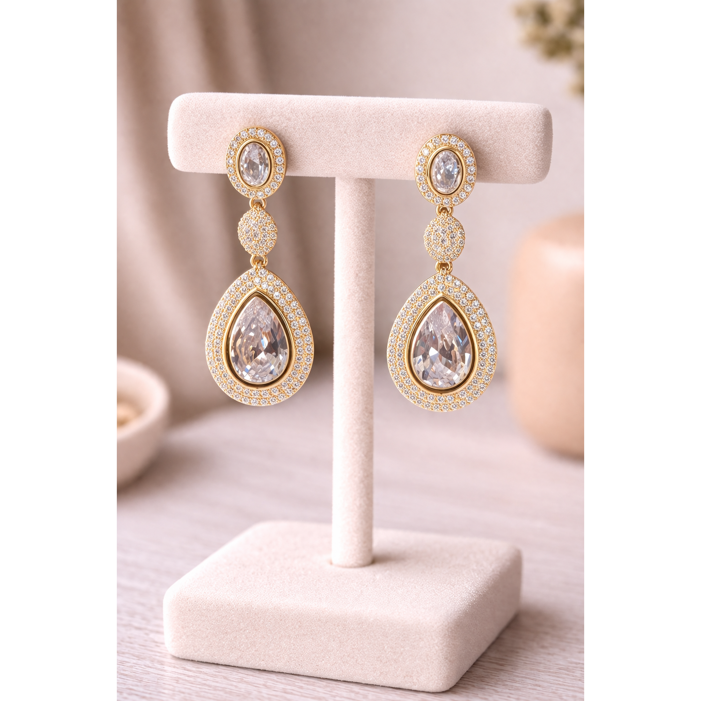 High-definition product photo of gold drop earrings with clear crystal stones displayed on a jewelry stand, featuring pavé detailing and a modern statement design.
