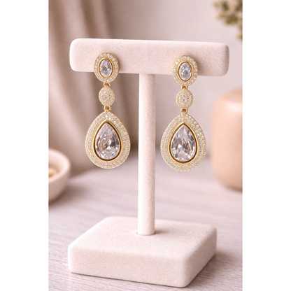 High-definition product photo of gold drop earrings with clear crystal stones displayed on a jewelry stand, featuring pavé detailing and a modern statement design.