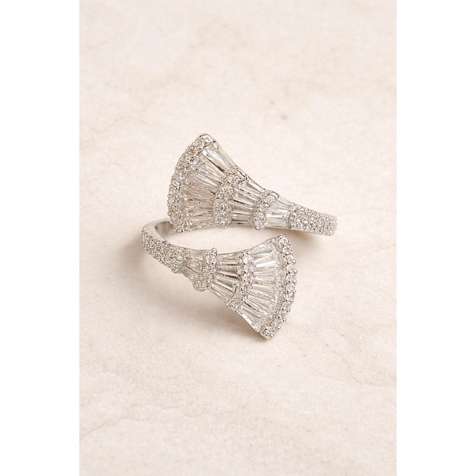 Silver fan-shaped baguette open wrap statement ring placed flat on light beige marble surface with soft studio lighting