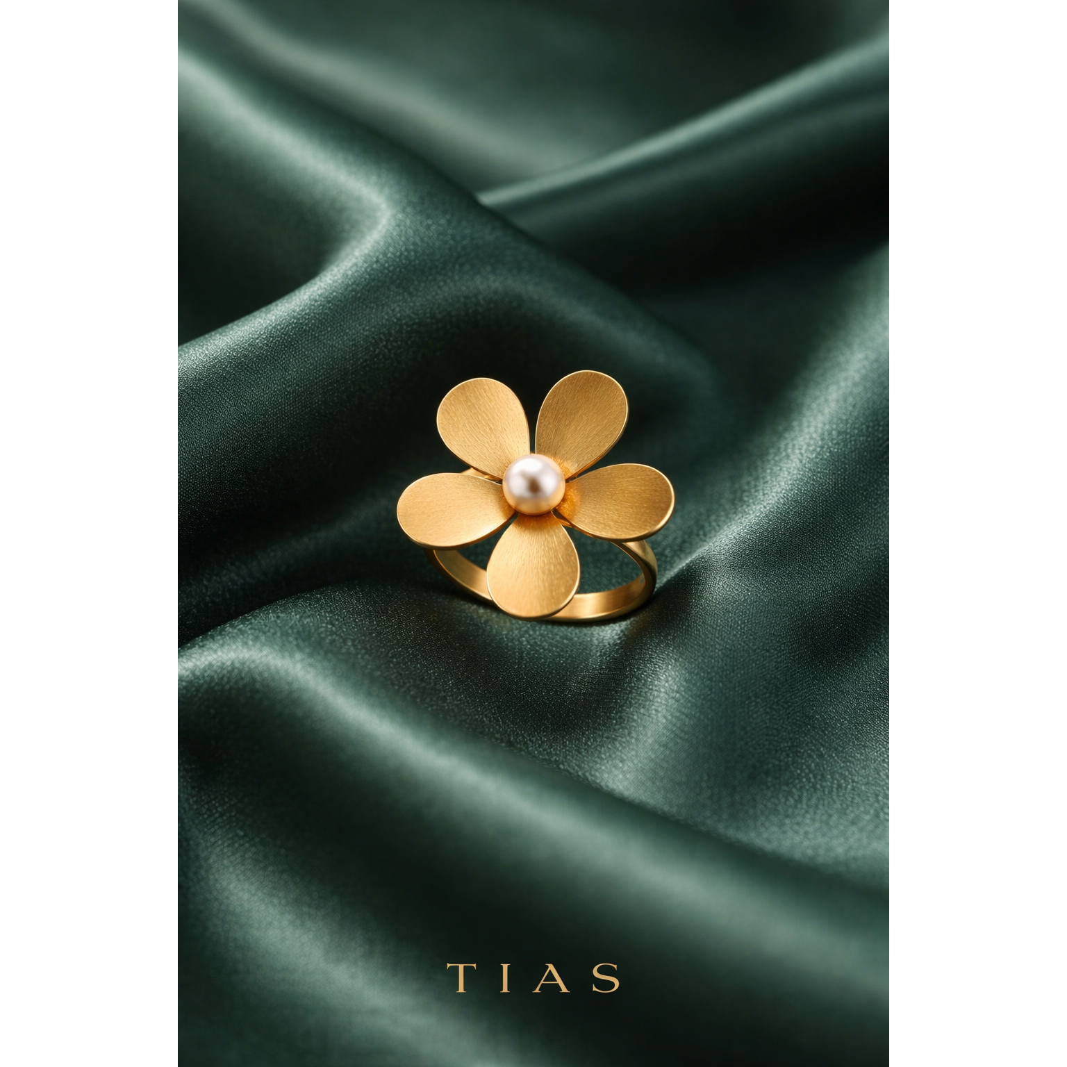 Gold flower-shaped ring with a pearl on a green satin background