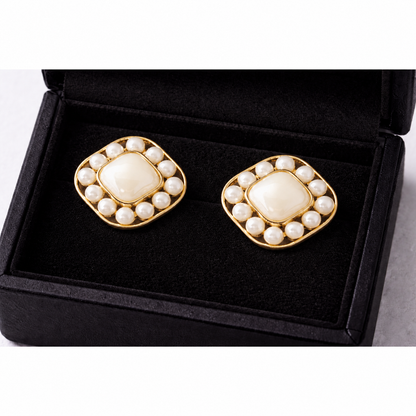 Gold pearl square stud earrings with mother-of-pearl center displayed inside a black velvet jewellery box, high-definition product photography.