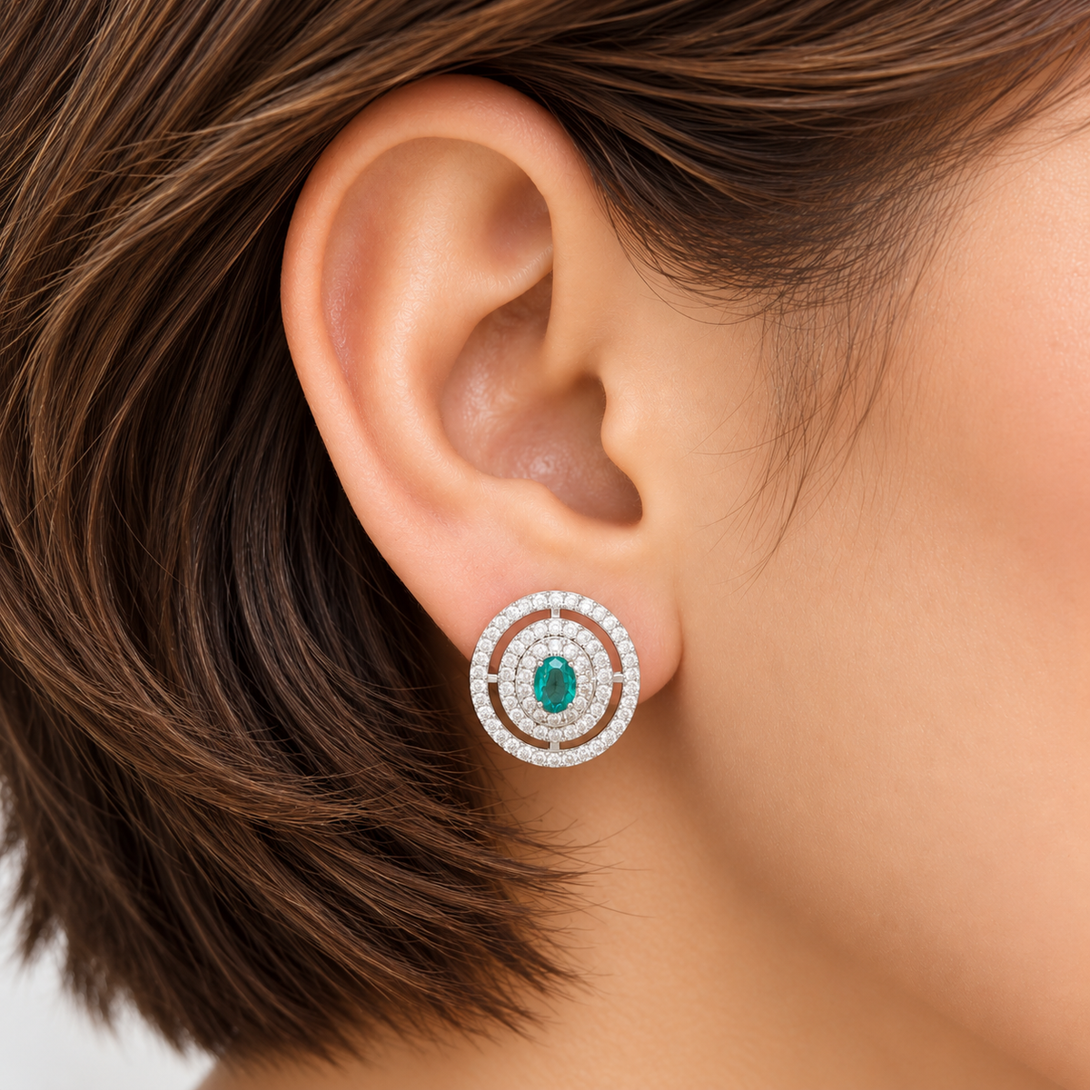 Close-up of an ear wearing Emerald Medallion Zircon Studs with a green oval gemstone and circular zircon detailing