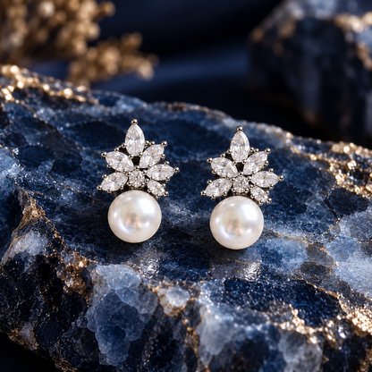 Pearl Crest Stud Earrings with round white pearls and marquise-cut clear zircon clusters in a polished silver-tone setting on blue stone