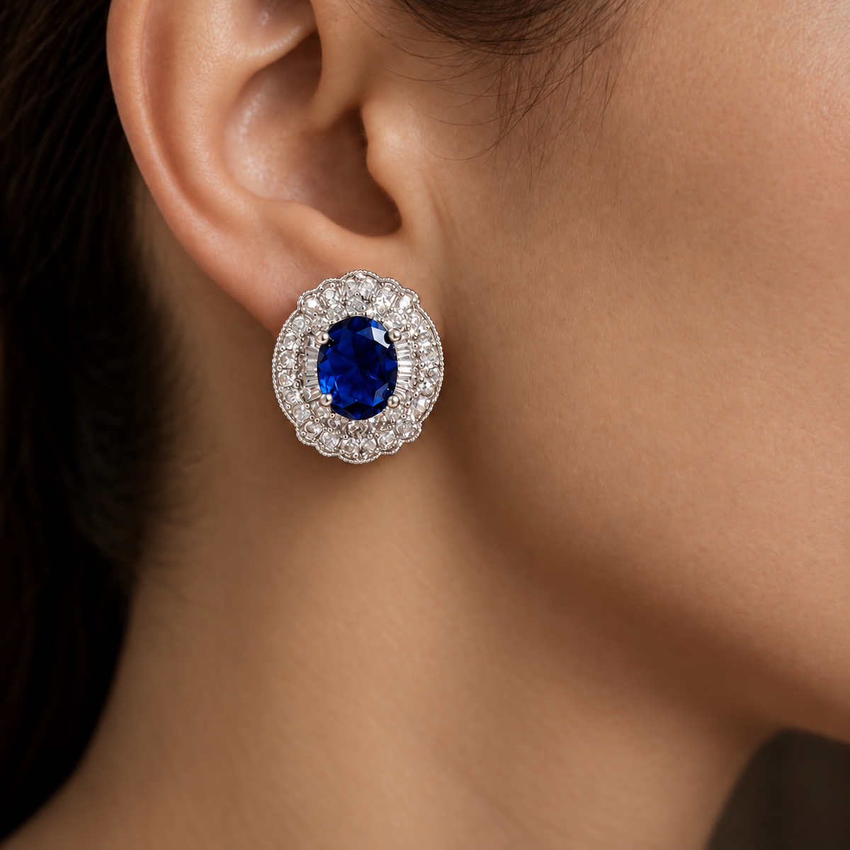 Close-up of Verdanza Oval Stud worn on the ear, featuring an sapphire blue oval centre stone surrounded by intricate clear zircon detailing.
