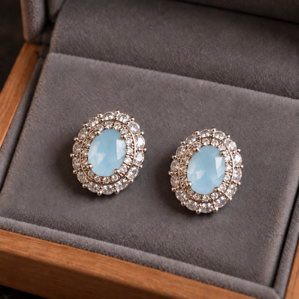Close-up of silver S925 stud earrings featuring faceted oval  sea blue centre stones with intricate clear zircon 
