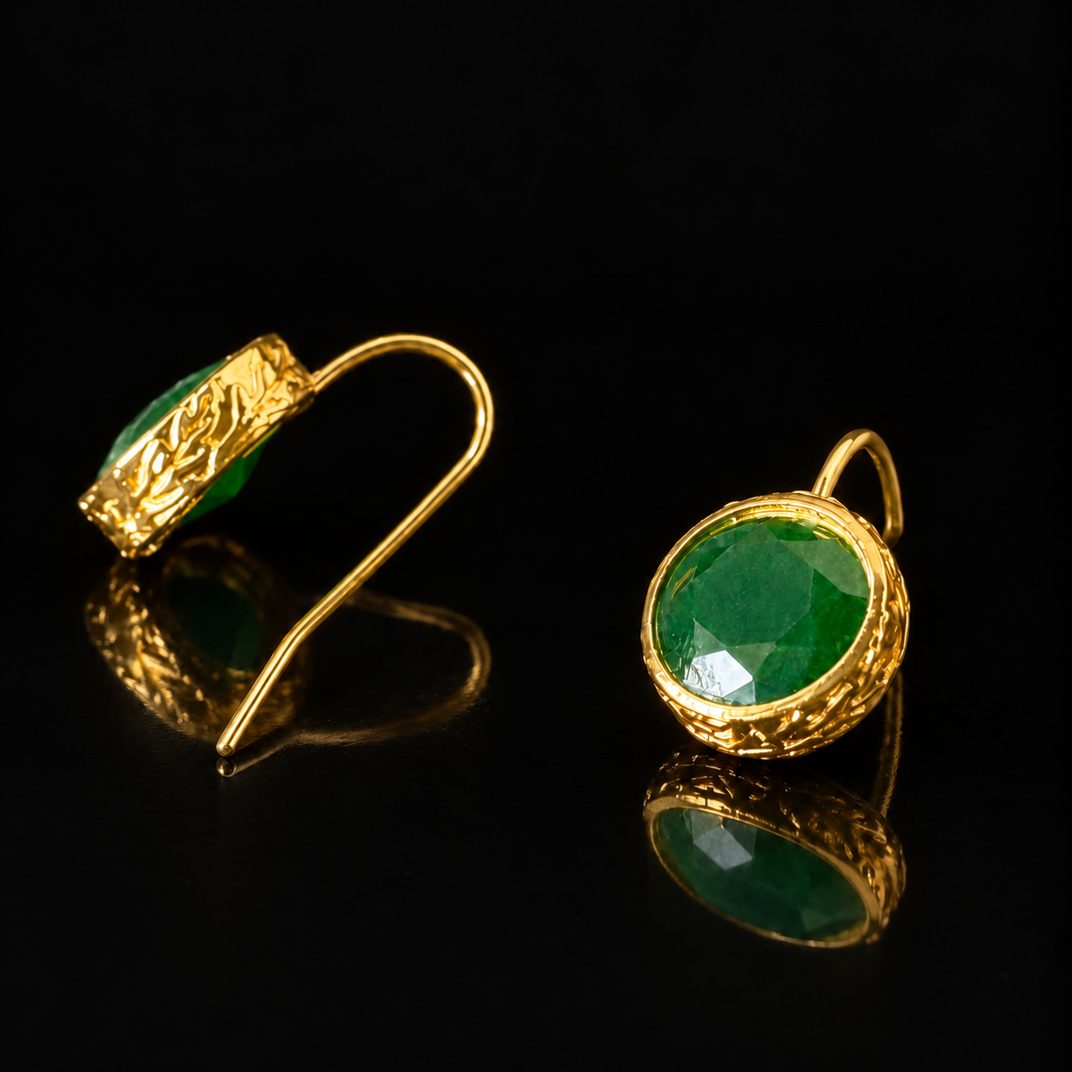 Verdant Relic Drop earrings from The Legacy Collection with round faceted emerald-green stones, textured gold-tone frames and long hook fastenings on a black reflective surface