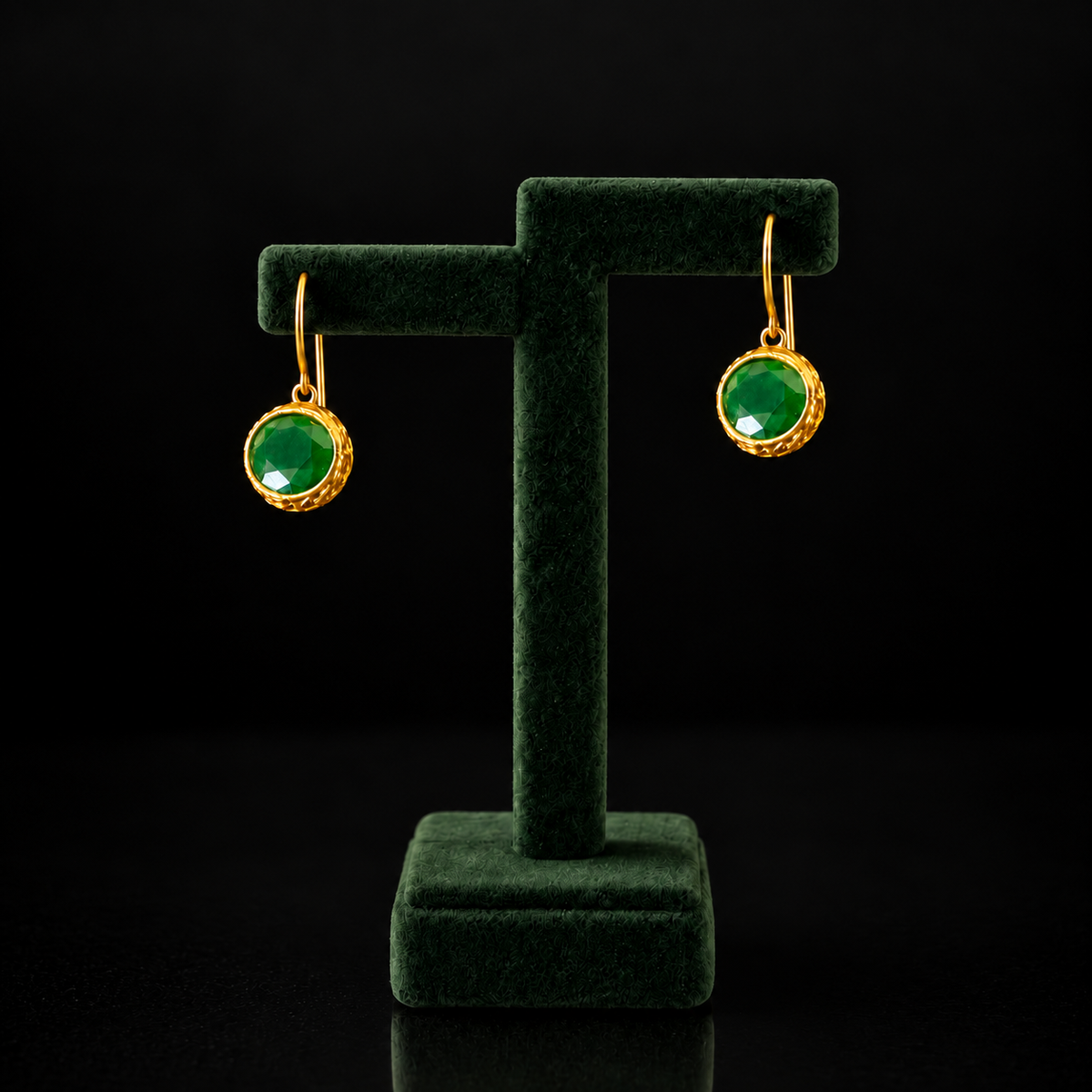 Pair of Verdant Relic Drop earrings from The Legacy Collection displayed on a deep green jewellery stand, featuring emerald-green stones and textured gold-tone settings