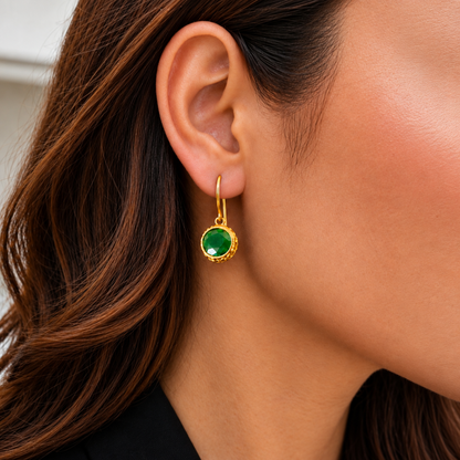 Close-up of a model wearing a Verdant Relic Drop earring with a faceted emerald-green round stone suspended from a slender gold-tone hoo