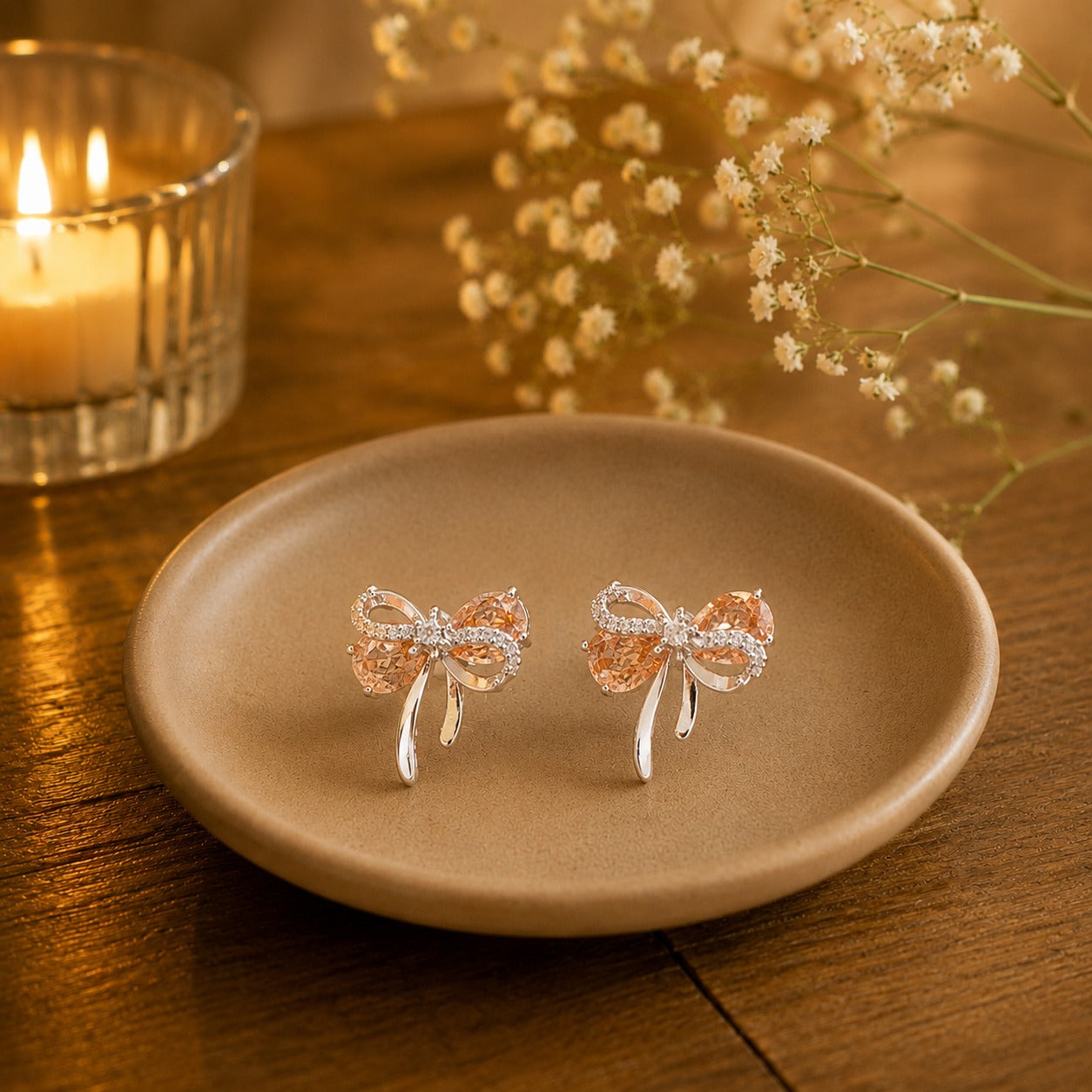 Champagne peach bow stud earrings on beige ceramic plate.