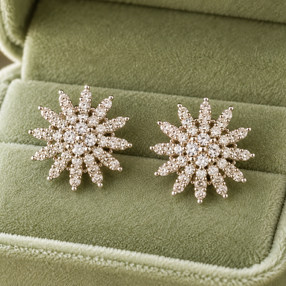 Crystal snowflake stud earrings displayed inside a sage green velvet jewelry box on a reflective table with soft natural light.
