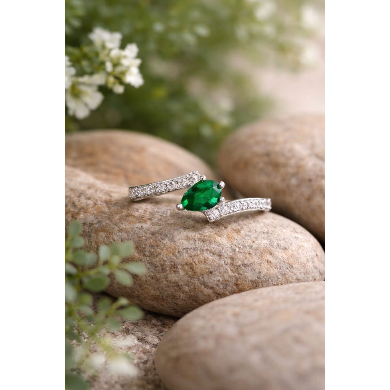 Silver ring with an emerald green gemstone on a stone surface with a natural background