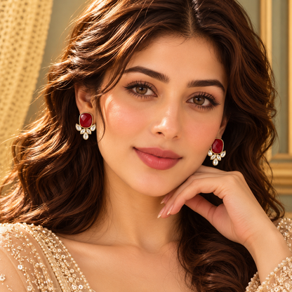 Model wearing Legacy Crownleaf Studs featuring a  ruby red cushion-shaped centre stone with clear leaf-cut accents in a polished gold-tone settin