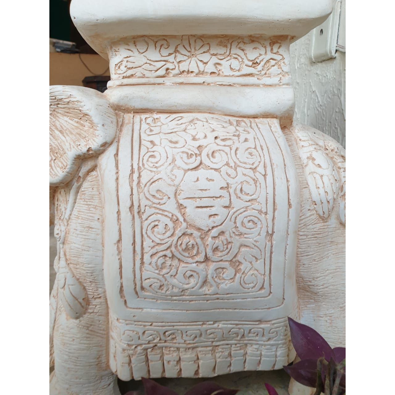 A close-up of a carved wooden pedestal with three elephant figures serving as legs, showcasing intricate details on their bodies and heads