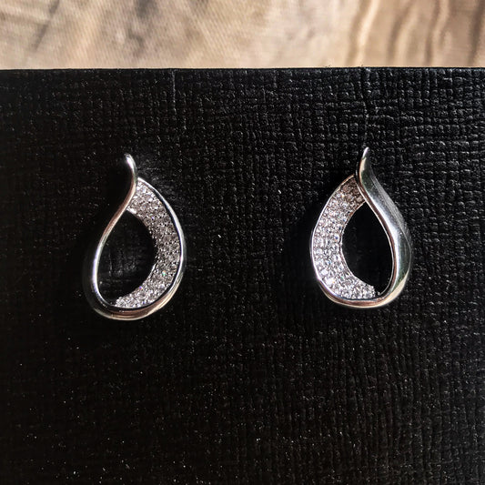 Two teardrop-shaped stud earrings, one silver and one gold, each with one side covered in sparkling clear stones, displayed on a black textured surface.