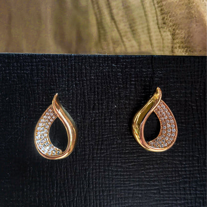 Two teardrop-shaped stud earrings, one silver and one gold, each with one side covered in sparkling clear stones, displayed on a black textured surface.