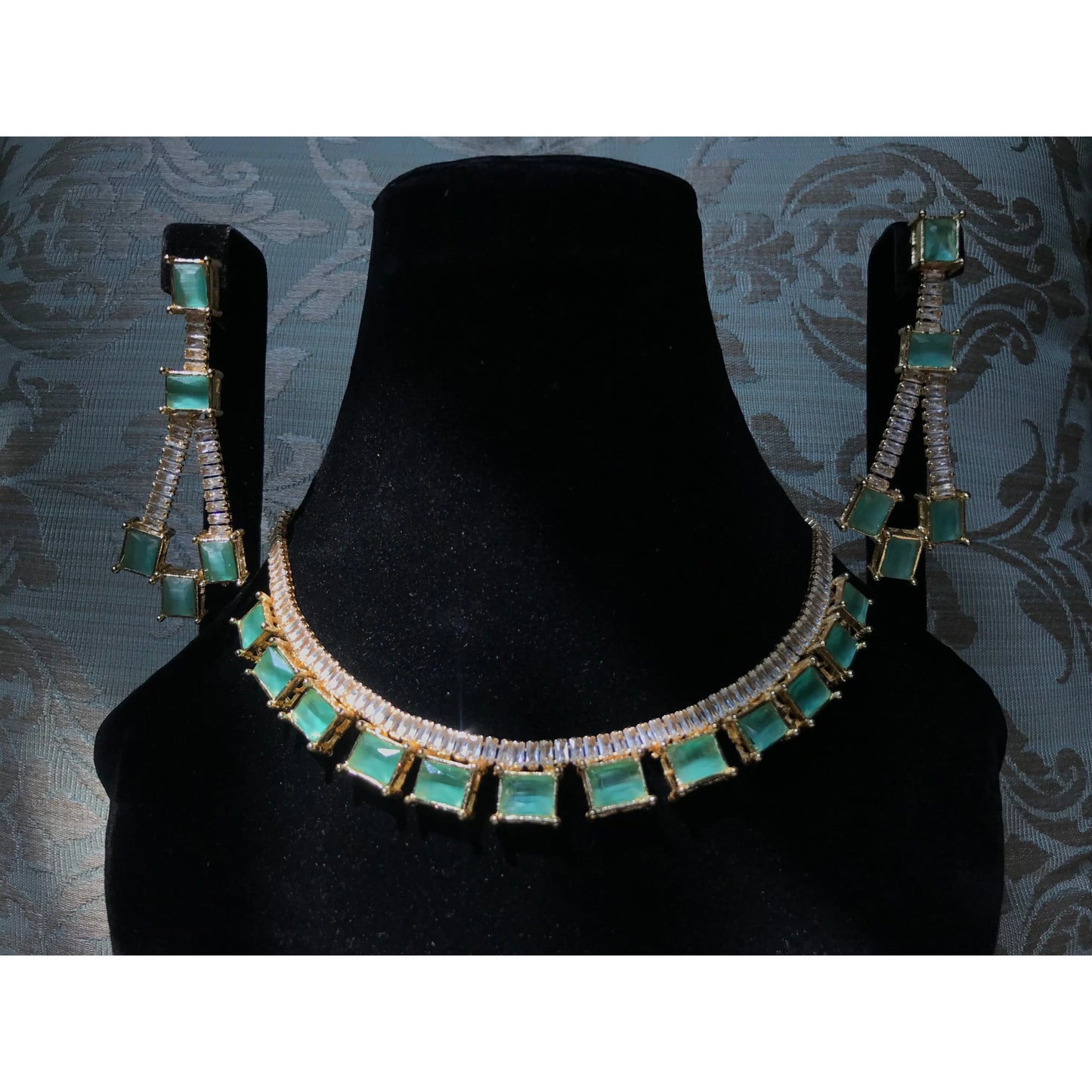 Jewelry set with necklace and earrings on a black stand against a patterned background