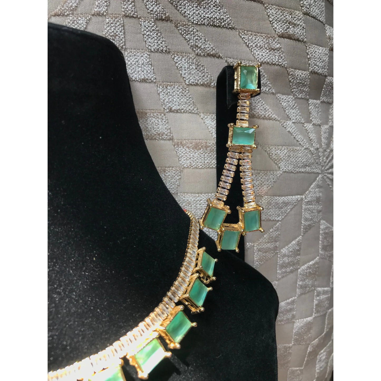 Necklace with green gemstones and gold accents on a black stand against a textured gray background