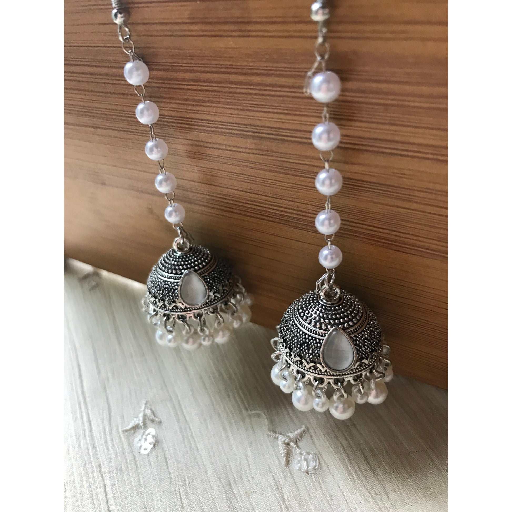 Pair of silver jhumkas with pearl-like beads on a wooden surface
