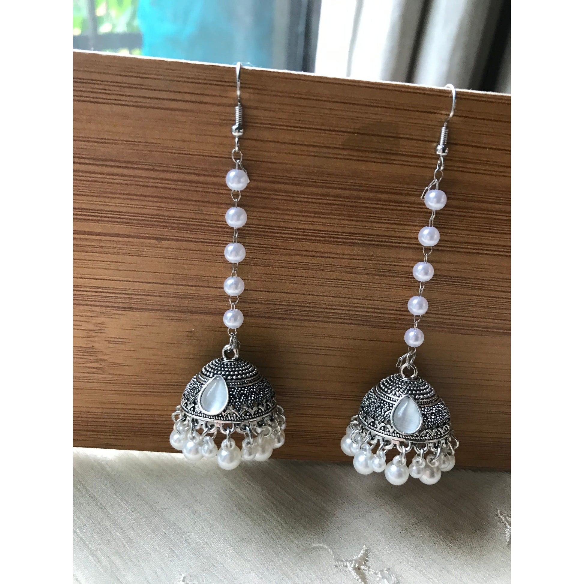 Pair of silver jhumkas with pearl-like beads on a wooden surface