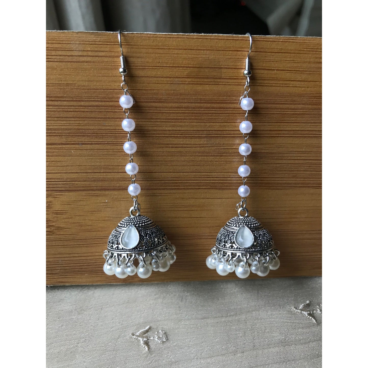Pair of silver jhumkas with pearl-like beads on a wooden surface