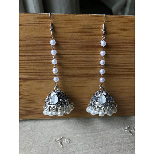 Pair of silver jhumkas with pearl-like beads on a wooden surface