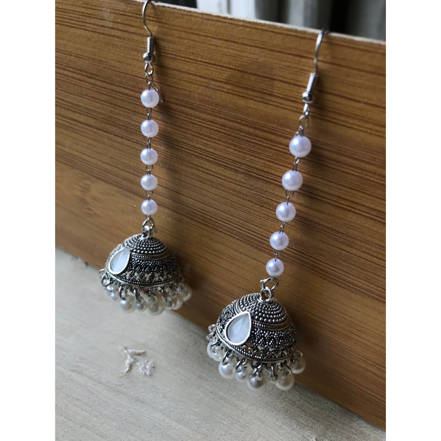 Pair of silver jhumkas with pearl-like beads on a wooden surface