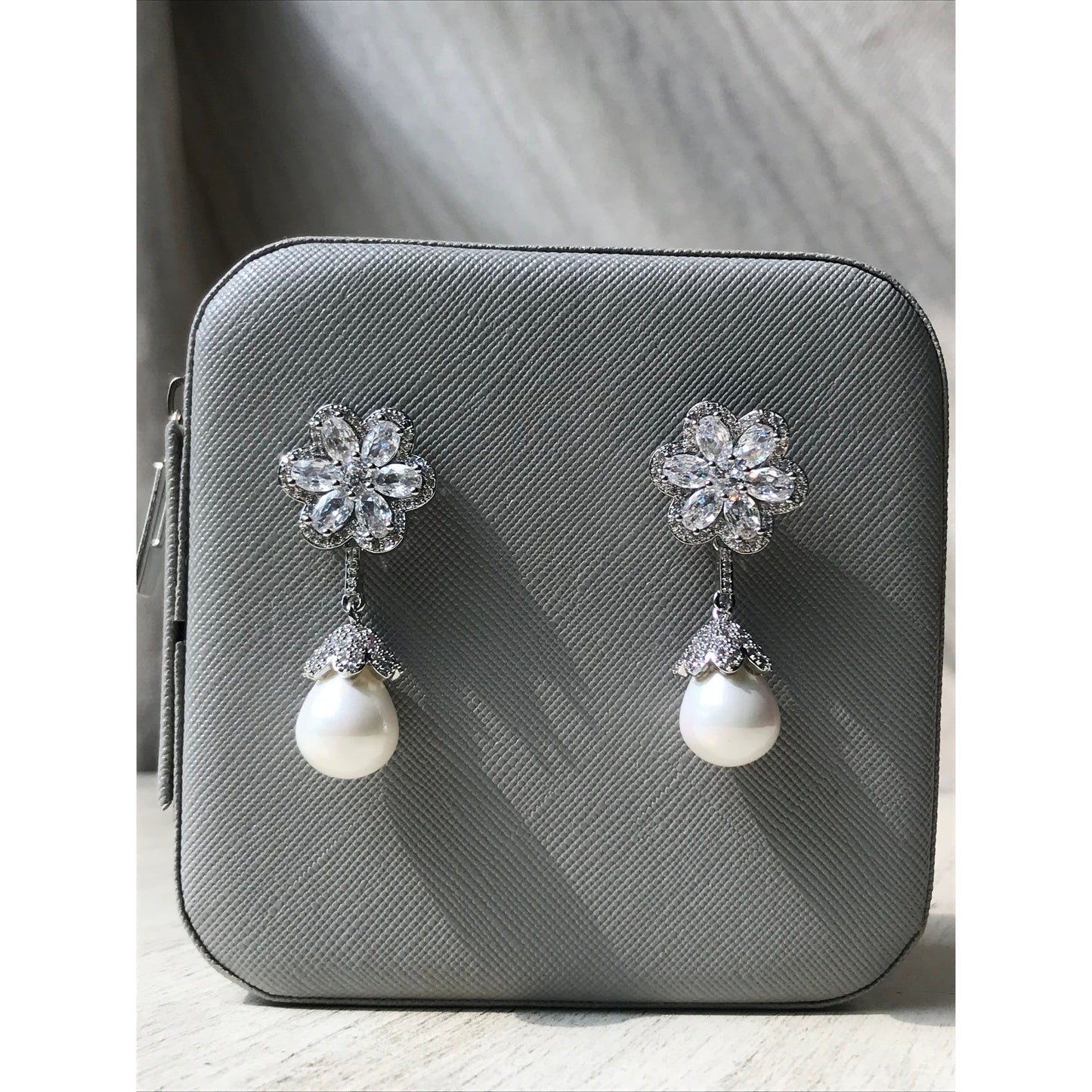 Pair of earrings with floral designs and pearls on a gray surface