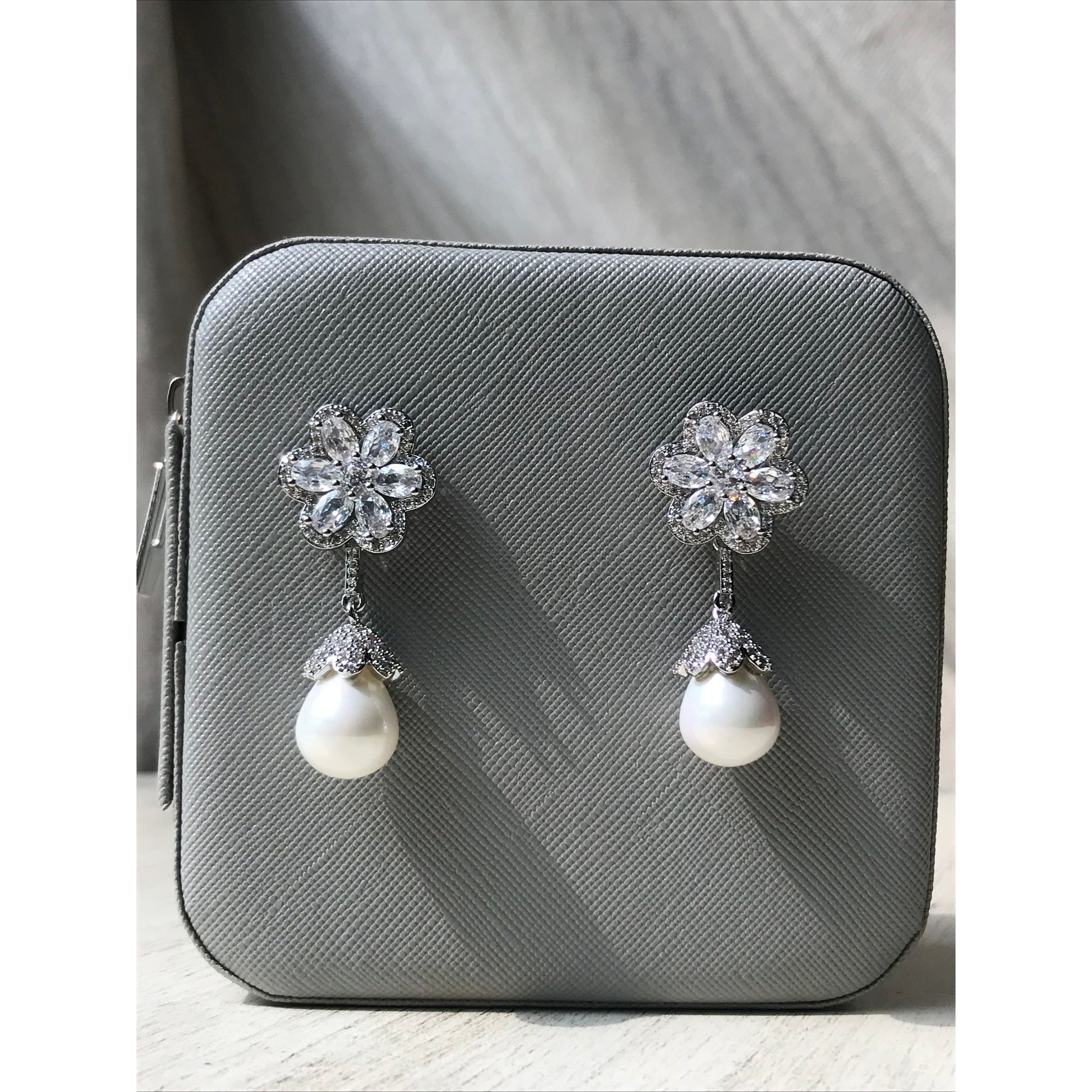 Pair of earrings with floral designs and pearls on a gray surface