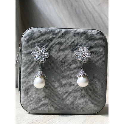 Pair of earrings with floral designs and pearls on a gray surface