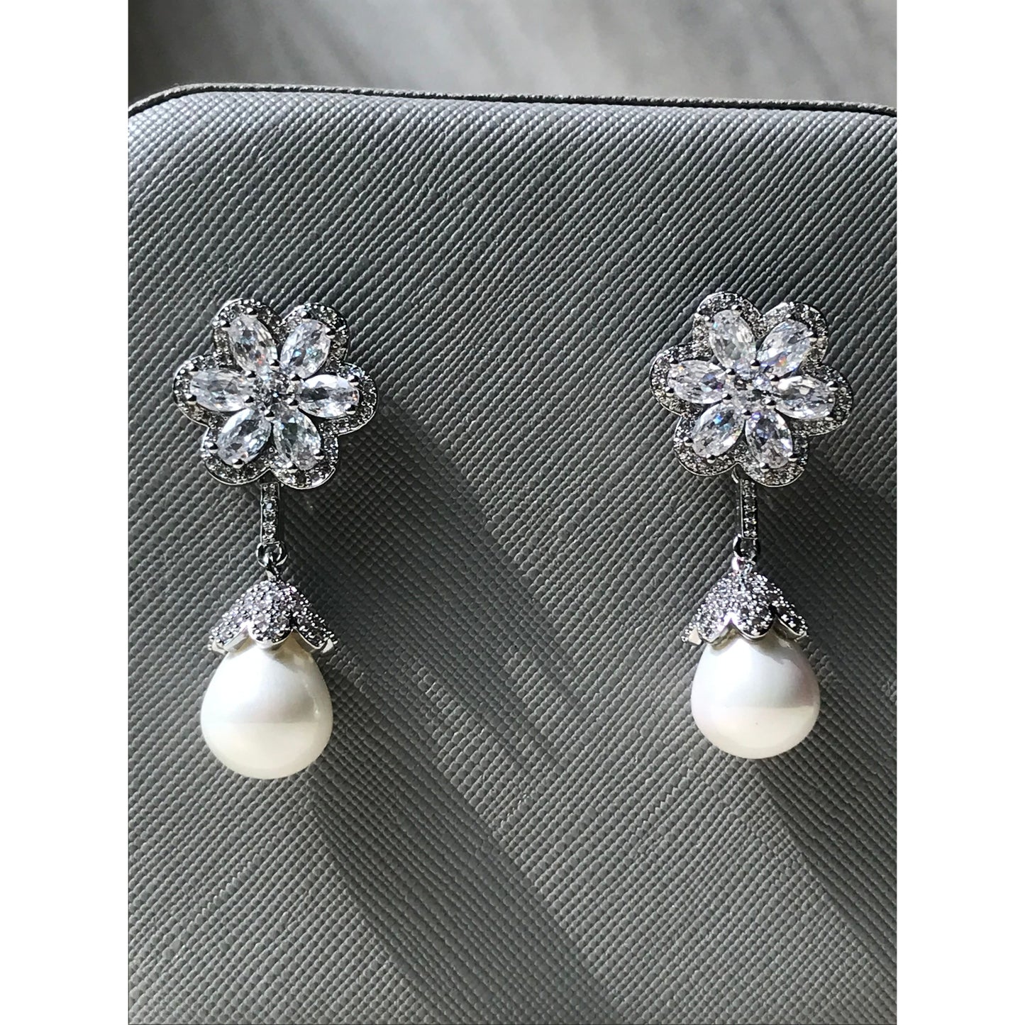 Pair of earrings with floral designs and pearls on a textured surface