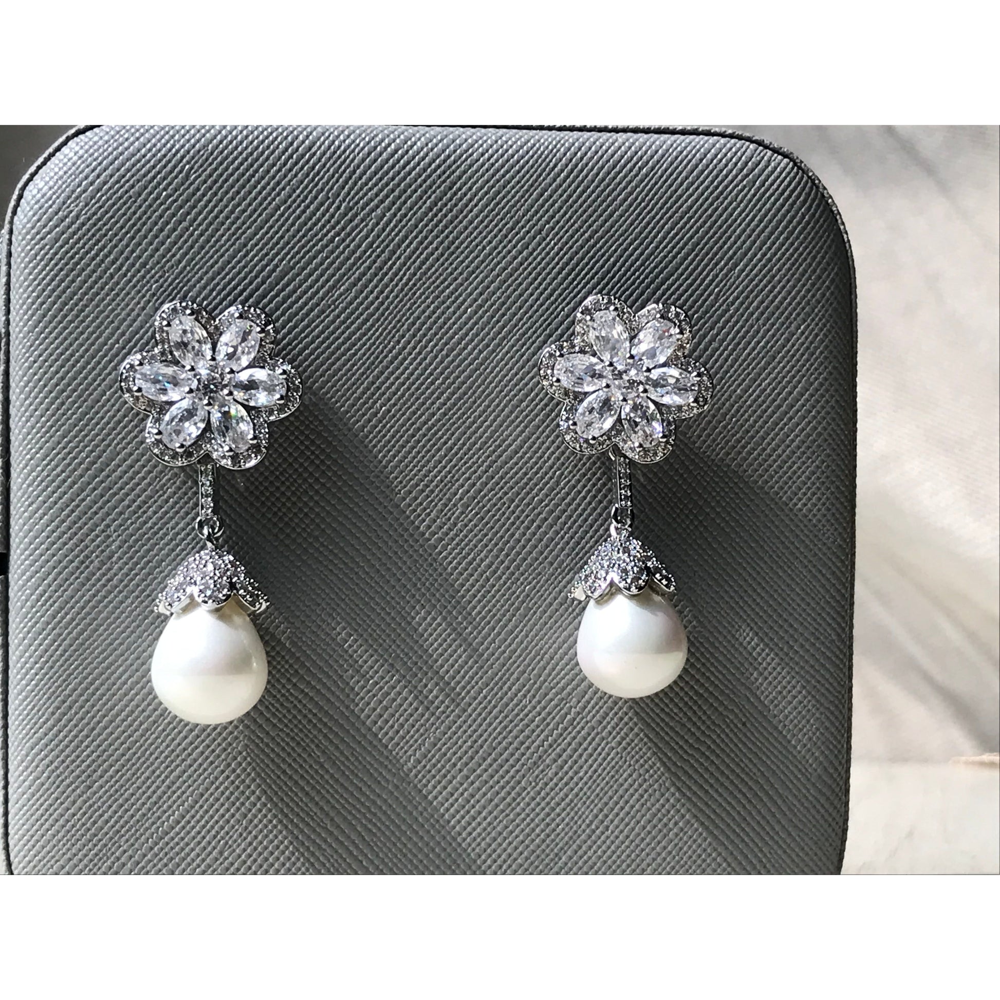 Pair of earrings with floral top and pearl drop on a gray textured background
