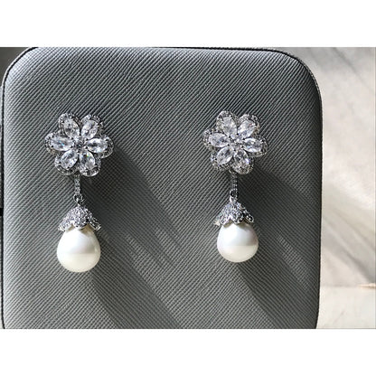 Pair of earrings with floral top and pearl drop on a gray textured background