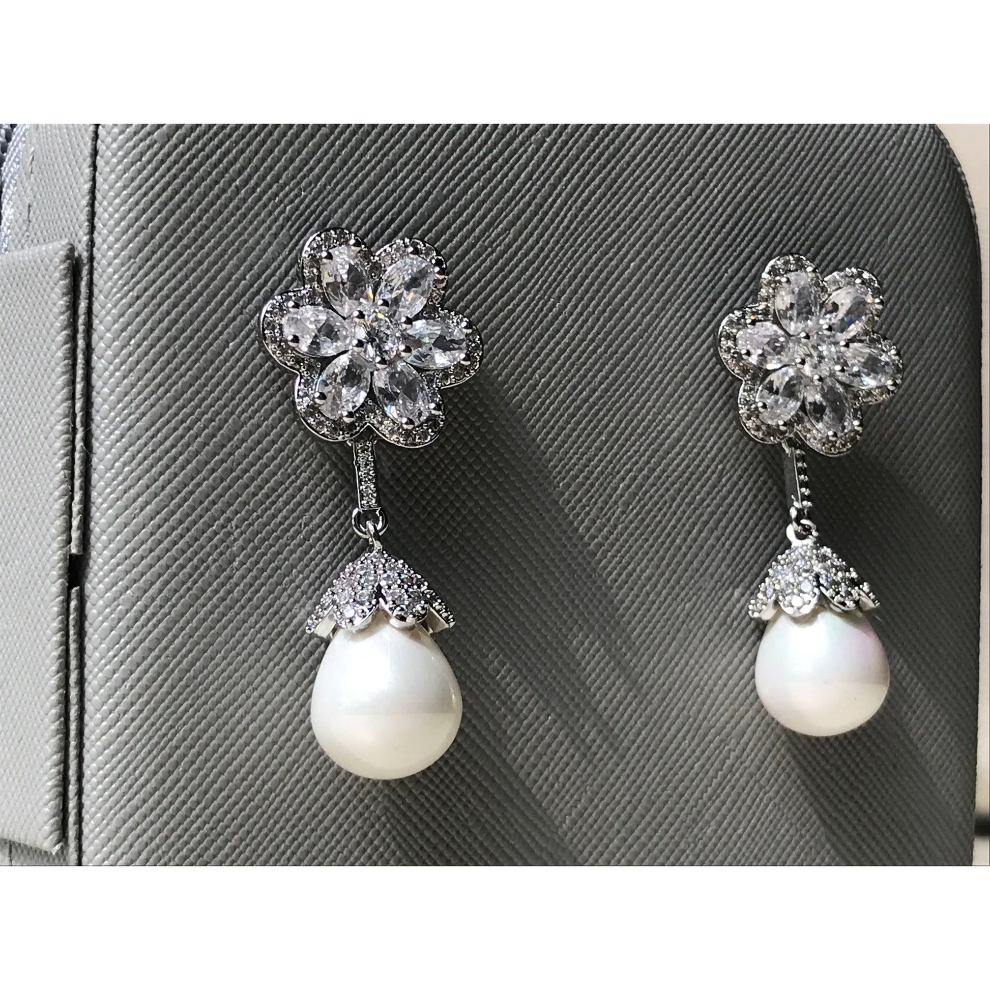 Pair of earrings with floral top and pearl drop on a gray textured background