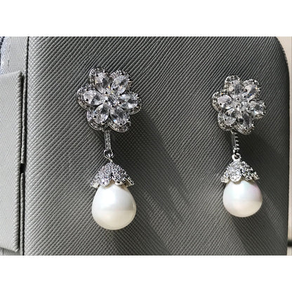 Pair of earrings with floral top and pearl drop on a gray textured background