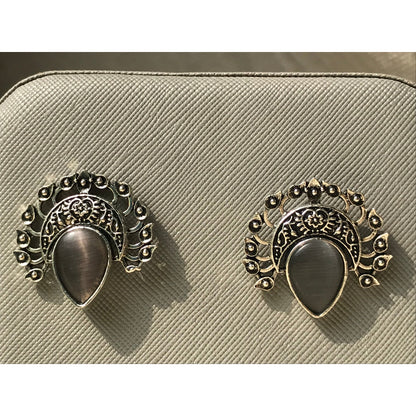 Pair of ornate earrings on a beige textured surface
