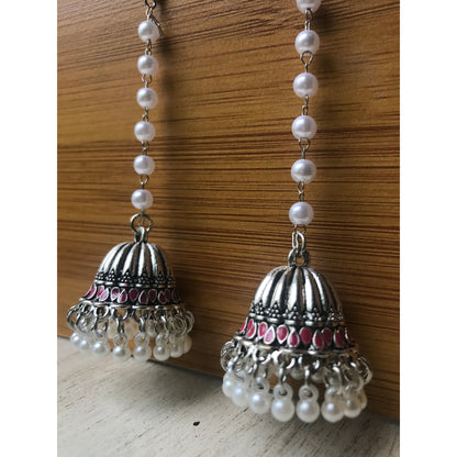 Pair of silver jhumka earrings with pink accents and pearl beaded chains hanging on a wooden backdrop against a white surface