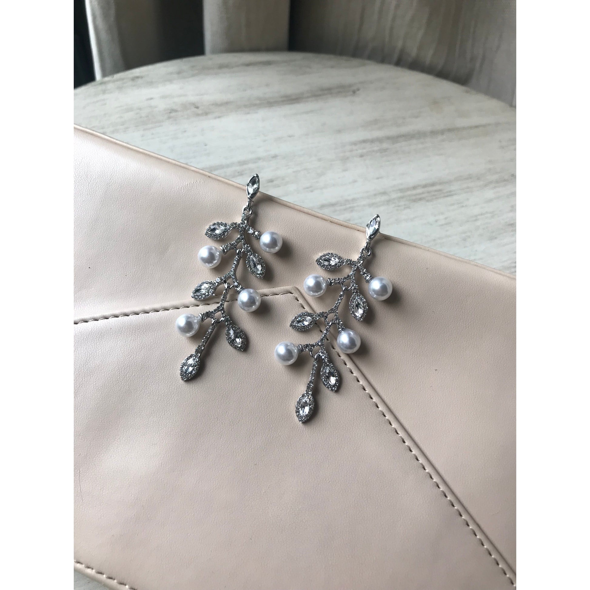 Pair of sparkling crystal leaf dangle earrings displayed on a gray jewelry case with a wood grain surface & curtain backdrop