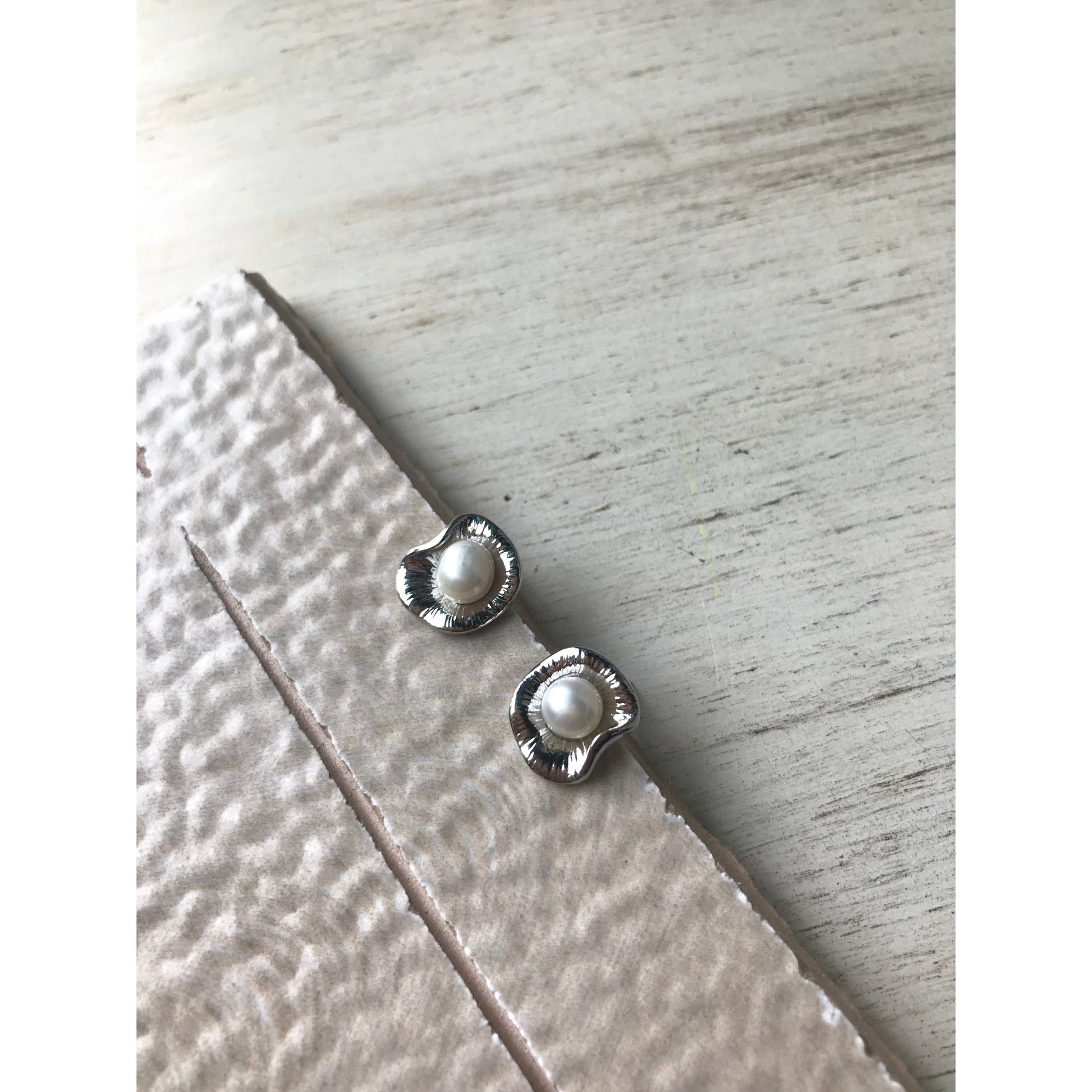 Silver earrings with a pearl on a light wooden surface