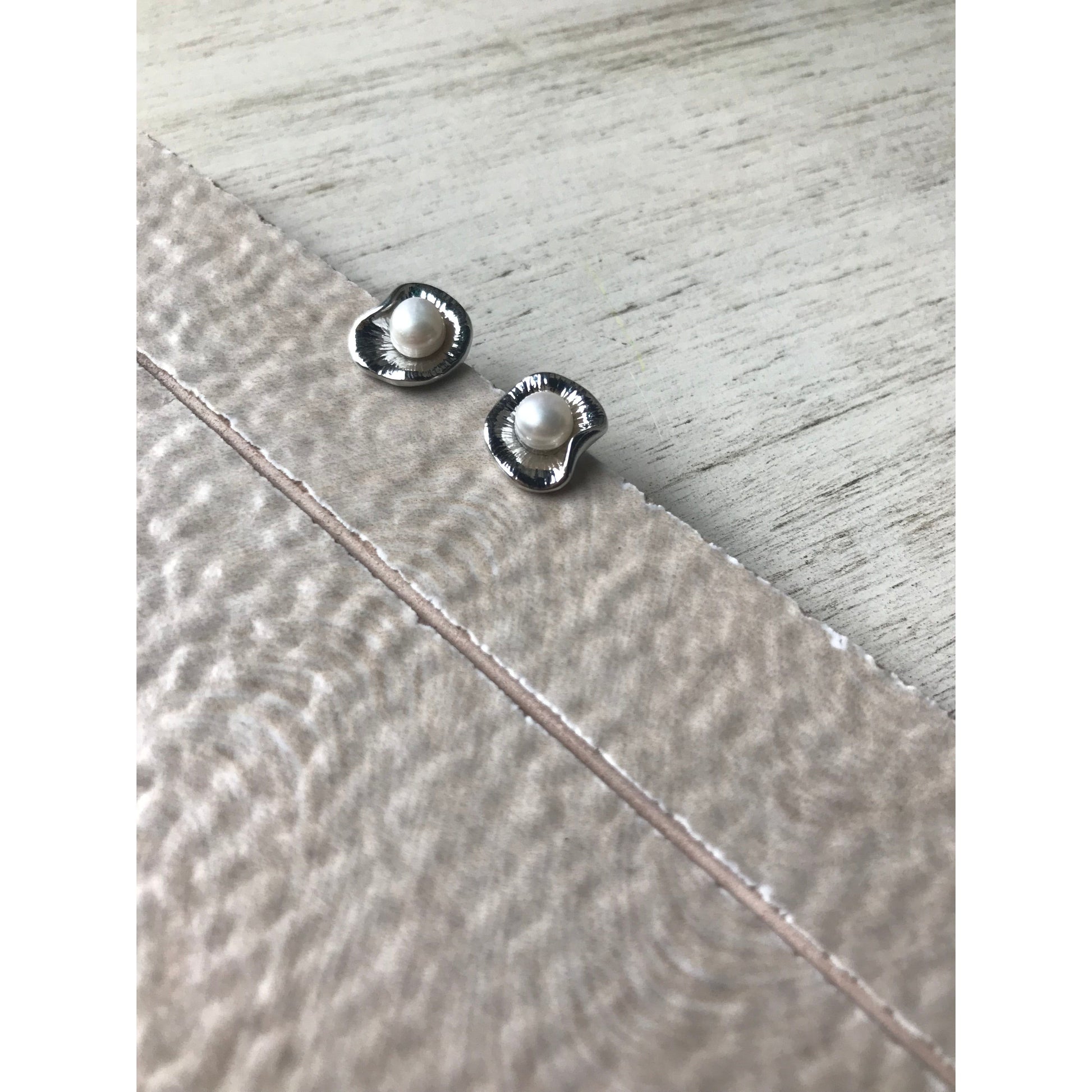 Two small silver earrings on a textured surface