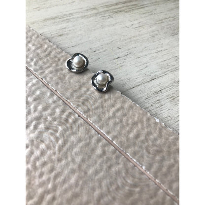 Two small silver earrings on a textured surface