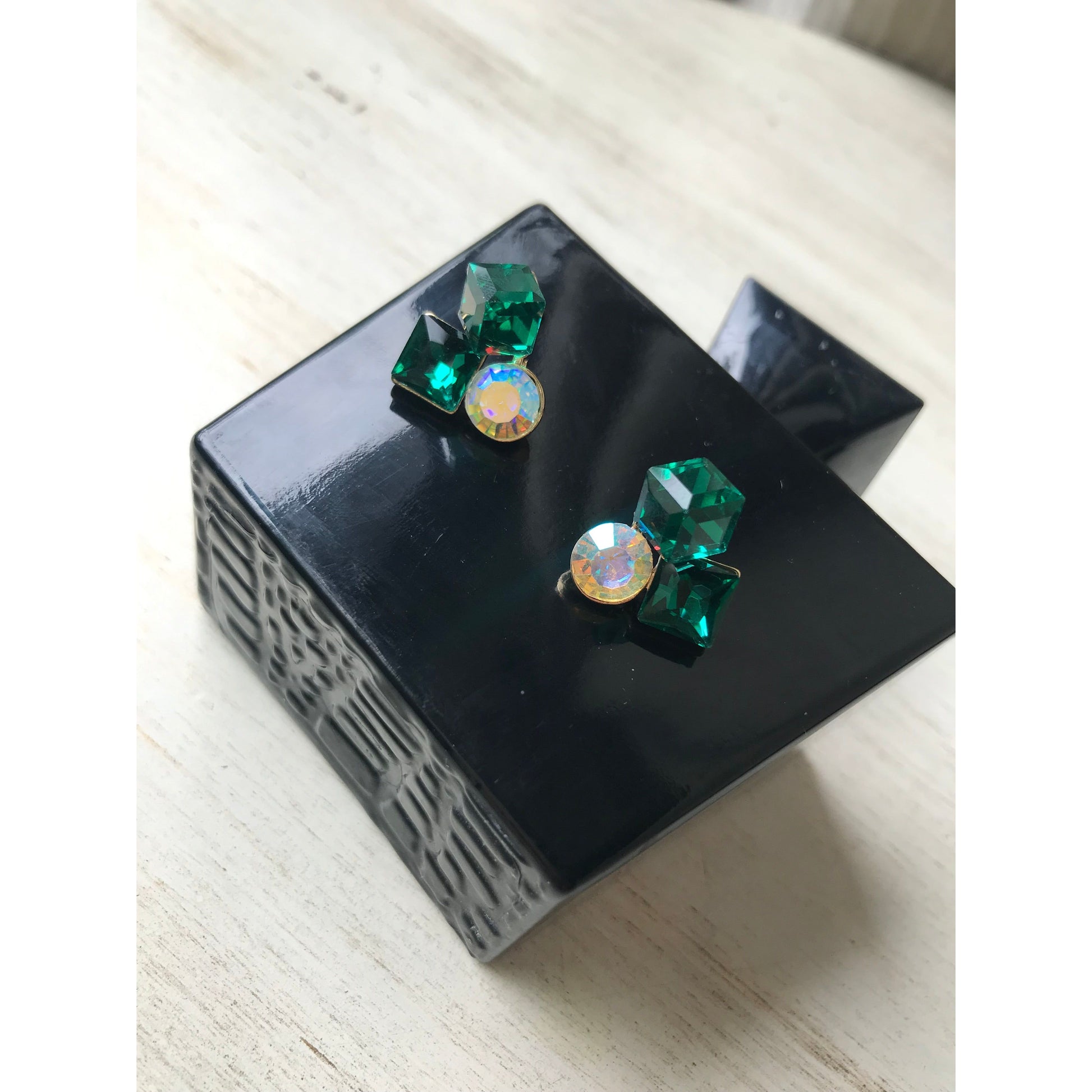 Green crystal earrings on a black box with a light wood background