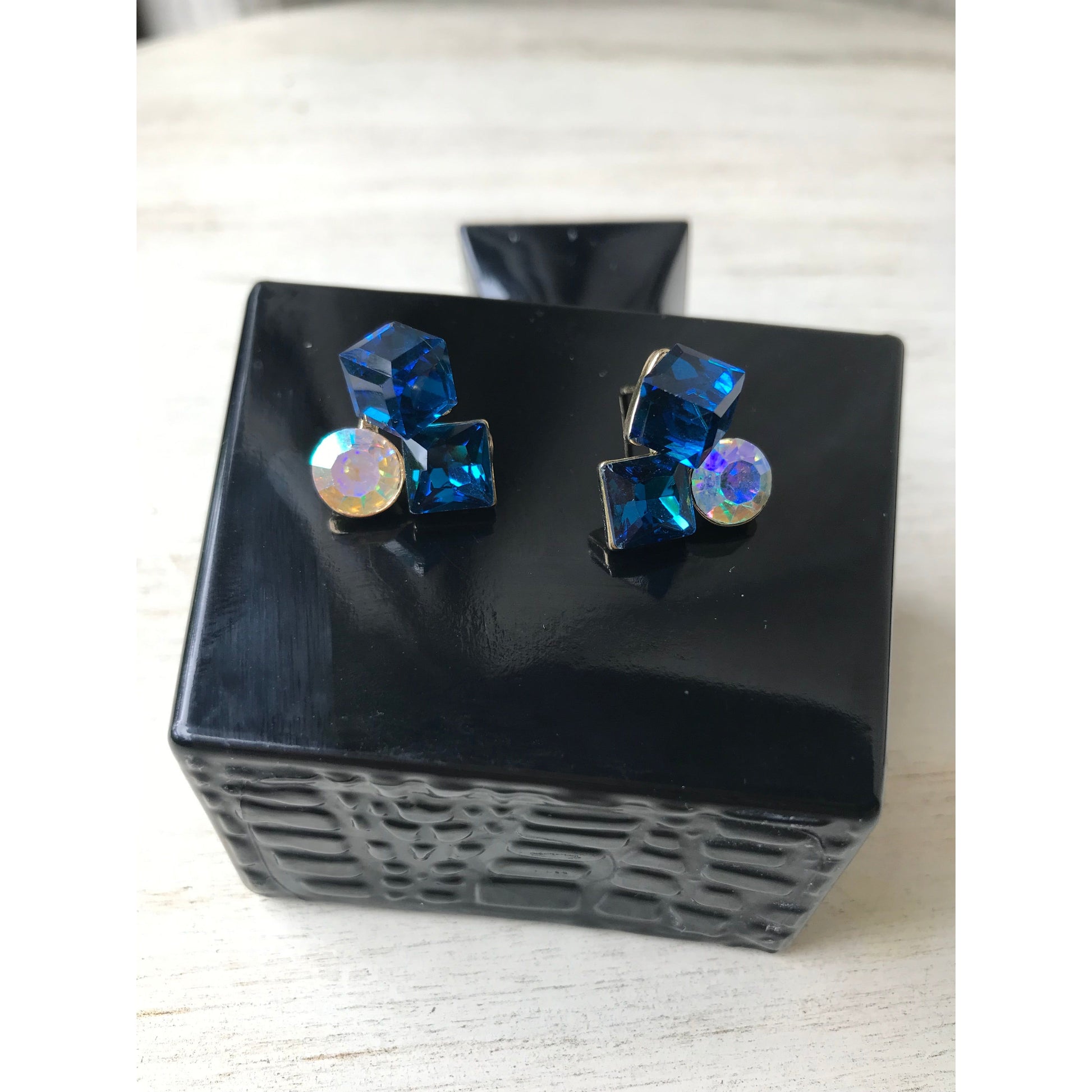 Blue gemstone earrings on a black stand with a white background