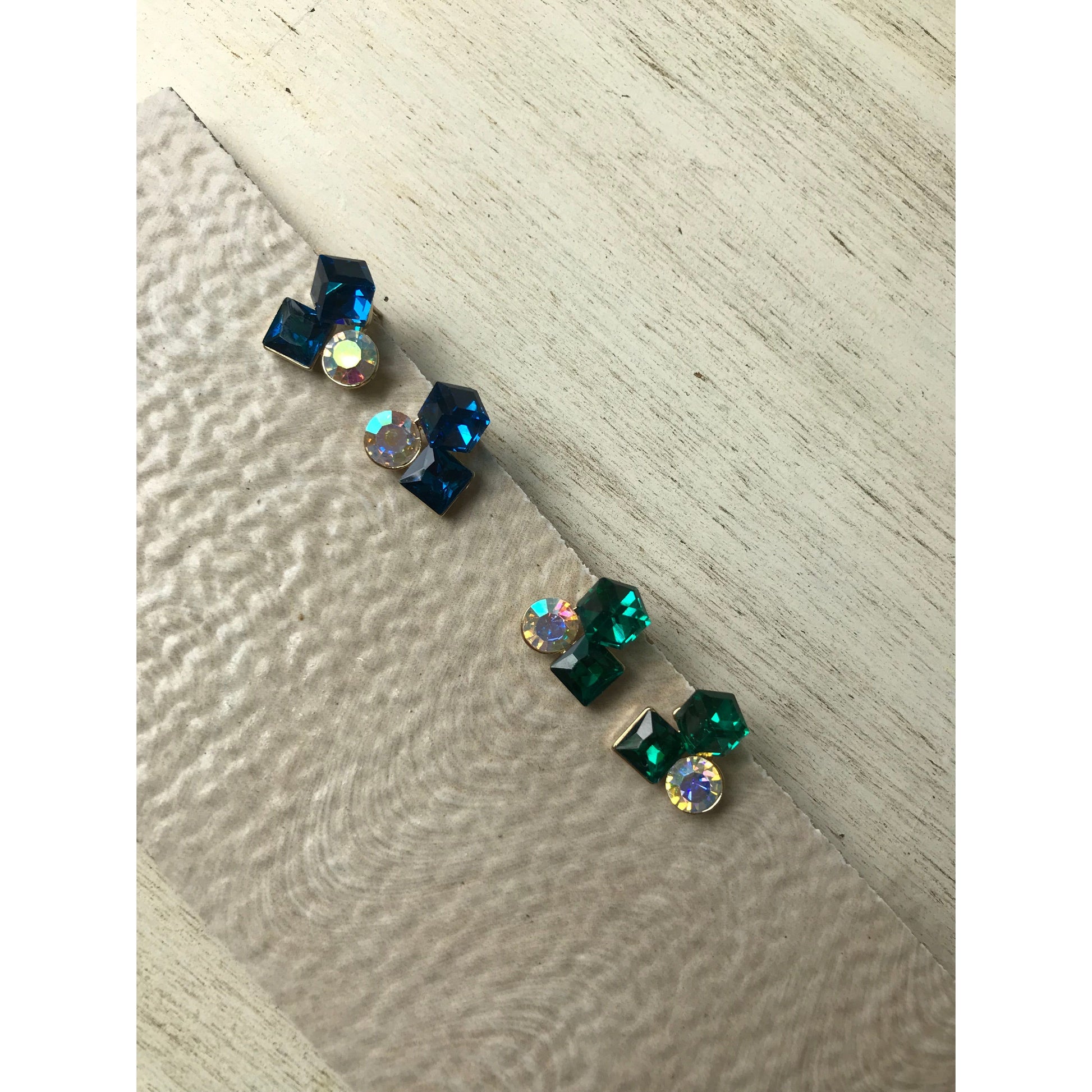 Pair of earrings with green and blue gemstones on a light wooden surface