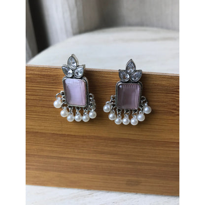 Pair of earrings with pink stones and pearl accents on a wooden surface