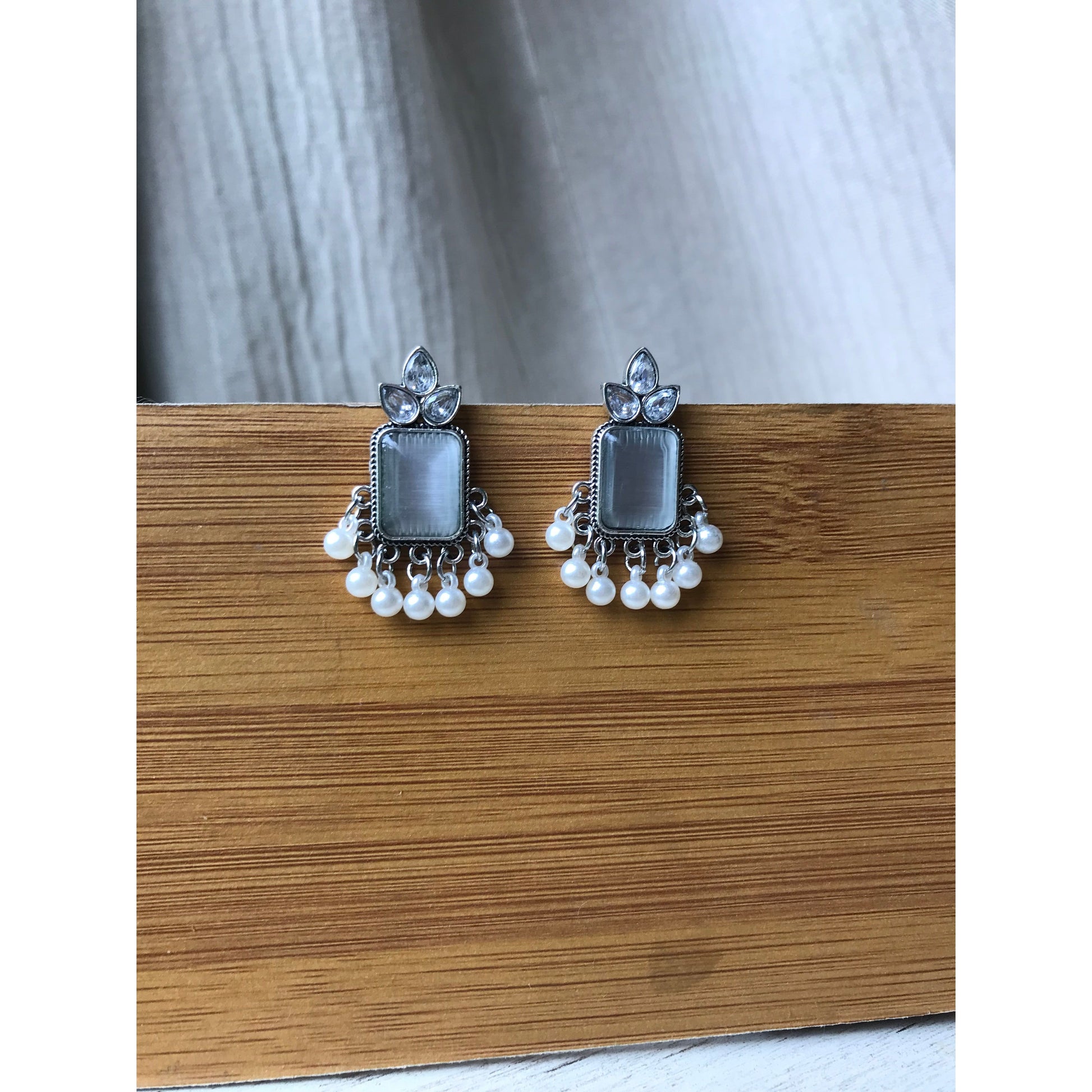 Pair of silver earrings with square stones and pearl-like accents on a wooden surface.